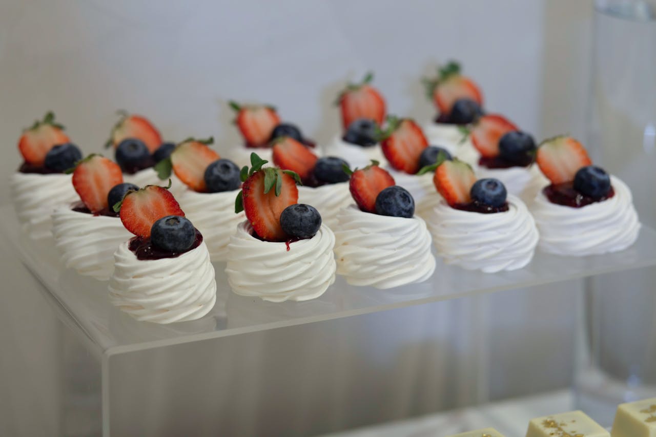 A visually appealing display of mini Pavlovas topped with strawberries and blueberries, perfect for events.